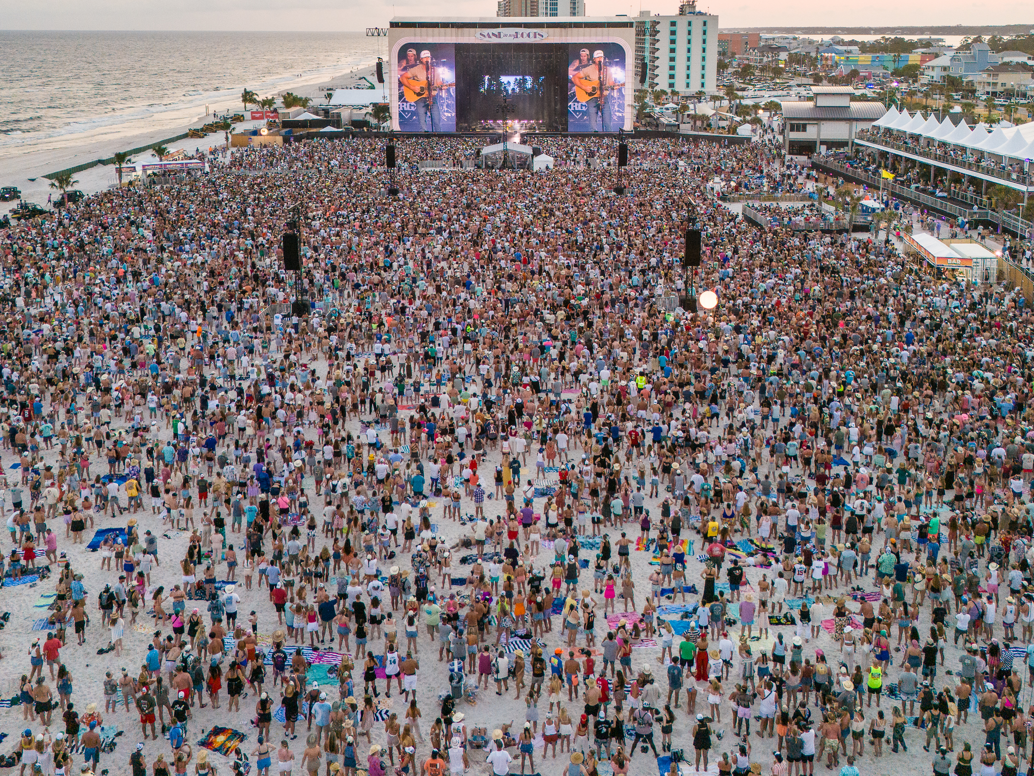 Sand in My Boots Festival crowd at sunset; large beachfront audience and main stage